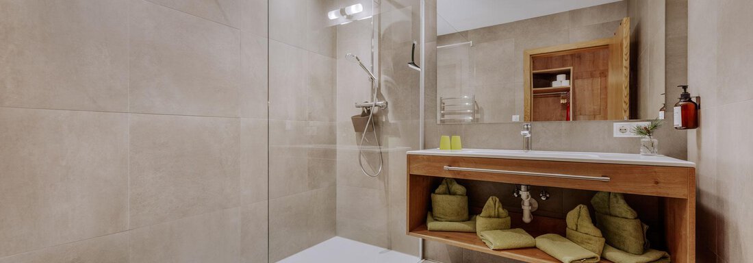 Ein modernes Badezimmer mit einer begehbaren Dusche und einer eleganten Holzablage. Die Wände sind in neutralen Farbtönen gehalten und die Handtücher sind ordentlich angeordnet. - Apartment Waldesruh - Ochsengarten