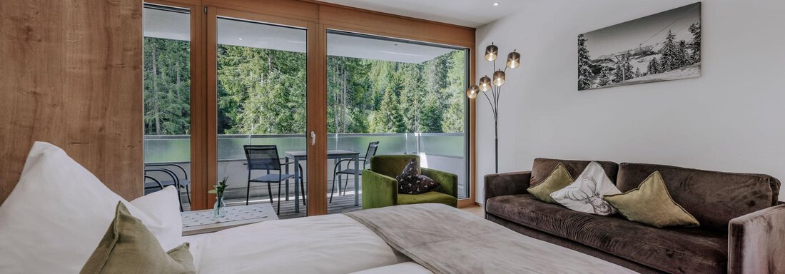 Ein modernes Zimmer mit zwei Betten und einem gemütlichen Sofa. Große Fenster bieten einen Blick ins Grüne. - Apartment Waldesruh - Ochsengarten