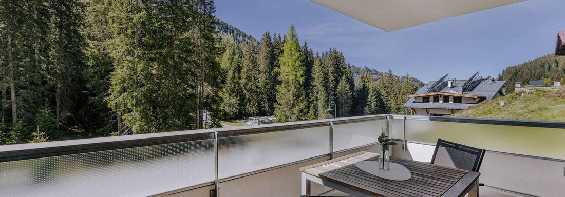 Ein schöner Balkon mit einem Tisch und Stühlen, umgeben von hohen Bäumen. Im Hintergrund sind weitere Gebäude und eine grüne Landschaft zu sehen. - Apartment Waldesruh - Ochsengarten