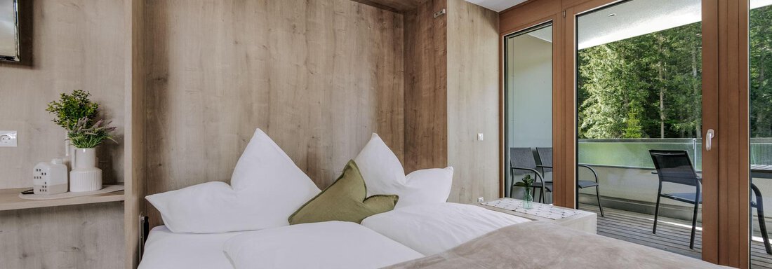 Ein modernes Zimmer mit einem Doppelbett und großen Fenstern. Der Blick führt auf eine entspannende Landschaft im Freien. - Apartment Waldesruh - Ochsengarten
