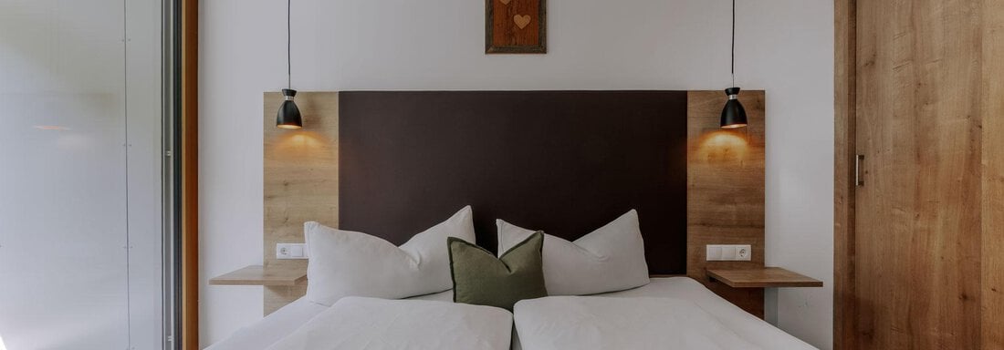 Ein modernes Schlafzimmer mit einem großen Doppelbett und weichen Kissen. An den Wänden hängen stilvolle Lampen und ein dekoratives Bild. - Apartment Waldesruh - Ochsengarten