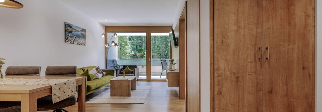 Ein modernes Wohnzimmer mit Holzfußboden und großen Fenstern. Es gibt einen Esstisch, eine bequeme Couch und einen Schrank aus Holz. - Apartment Waldesruh - Ochsengarten