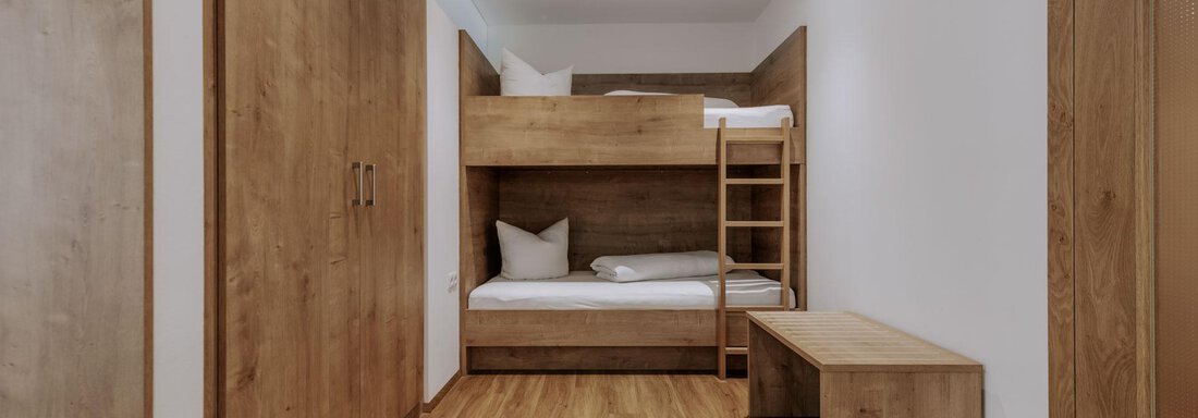 Ein einfaches Schlafzimmer mit einem Etagenbett aus Holz. Der Boden ist aus Holz, und es gibt eine gemütliche Sitzbank. - Apartment Waldesruh - Ochsengarten