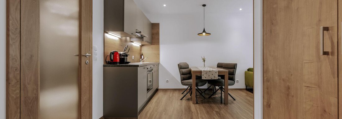 Ein moderner Wohnraum mit einer offenen Küche und einem Essbereich. Der Boden ist aus Holz und die Wände sind hell gestrichen. - Apartment Waldesruh - Ochsengarten