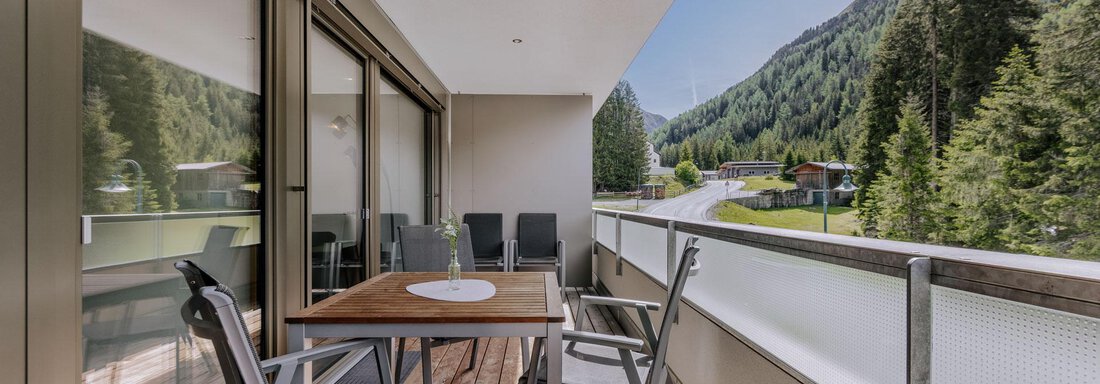 Ein moderner Balkon mit einem Holztisch und Stühlen. Blick auf eine grüne Berglandschaft und einen klaren blauen Himmel. - Apartment Waldesruh - Ochsengarten