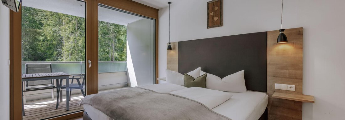 Ein modernes Schlafzimmer mit einem großen Doppelbett und holzwarmem Boden. Es gibt Zugang zu einem Balkon mit Blick auf die Natur. - Apartment Waldesruh - Ochsengarten
