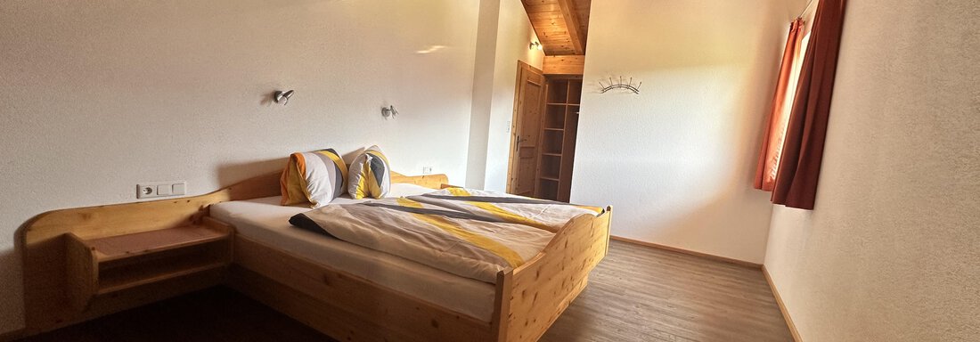 A bright bedroom with a large wooden double bed. Large windows provide plenty of daylight and a cozy atmosphere. - Ferienhaus Föger - Ochsengarten