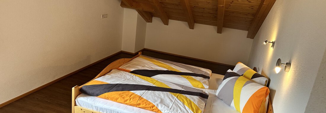 A cozy bedroom with a wooden ceiling and a double bed. The comforter has a modern, colorful pattern. - Ferienhaus Föger - Ochsengarten