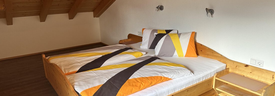 A cozy bedroom with a wooden bed and colorful bedding. The wooden beam ceiling creates a warm atmosphere. - Ferienhaus Föger - Ochsengarten