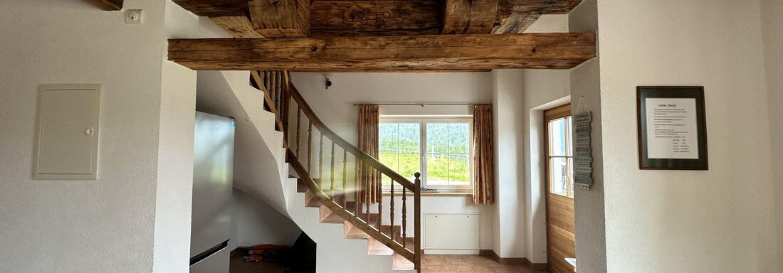 A spacious living room with a wooden ceiling and a staircase. Large windows provide plenty of light and a view of nature. - Ferienhaus Föger - Ochsengarten