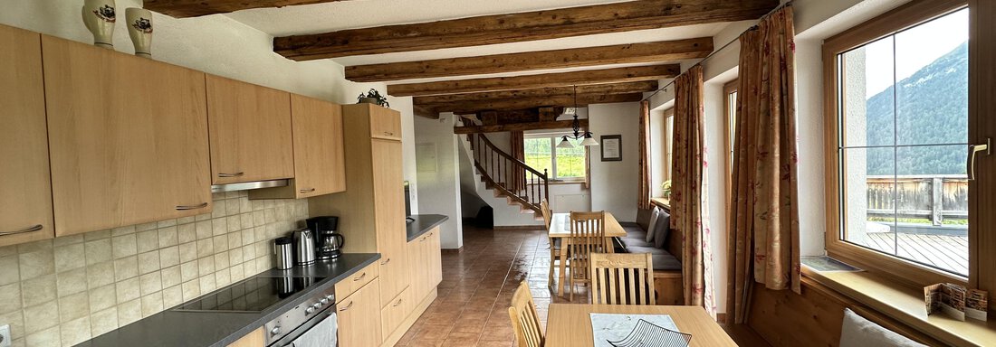 Wohnküche A modern kitchen with wooden ceiling beams and large windows. The dining area is bright and inviting, with a table and chairs. - Ferienhaus Föger - Ochsengarten