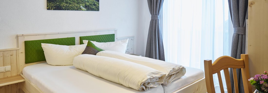 Ein gemütliches Schlafzimmer mit einem großen Bett und hellen Vorhängen. An der Wand hängt ein Bild von einer Berglandschaft. - Gasthof Walderhof - Ochsengarten