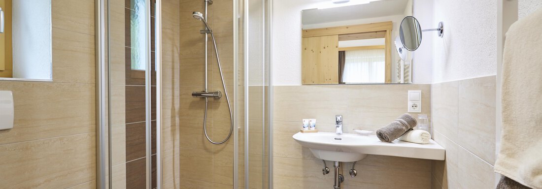 Ein modernes Badezimmer mit eine Dusche und einem Waschbecken. Die Wände sind in neutralen Farben gehalten, und es gibt ein großes Spiegel. - Gasthof Walderhof - Ochsengarten