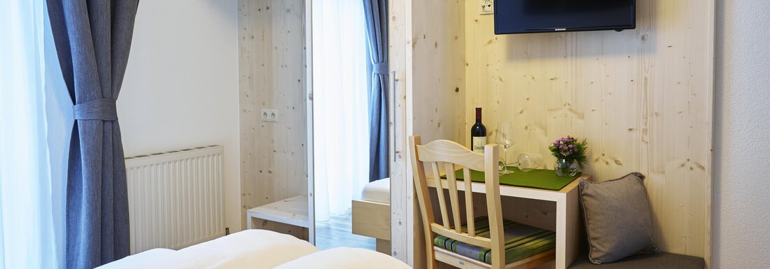 Ein modernes Zimmer mit zwei Betten, einem Tisch und einem Fernseher. Es gibt einen Kleiderschrank und ein Fenster mit Vorhängen. - Gasthof Walderhof - Ochsengarten
