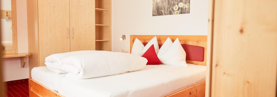 Ein gemütliches Schlafzimmer mit einem großen Bett und Holzschränken. Die Wände sind hell, und ein Bild von Blumen hängt über dem Bett. - Gasthof Walderhof - Ochsengarten