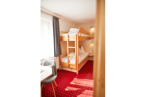 Ein einfaches Hotelzimmer mit einem Etagenbett und einem Einzelbett. Der Raum hat einen roten Teppich und einen kleinen Tisch mit einem Stuhl. - Gasthof Walderhof - Ochsengarten