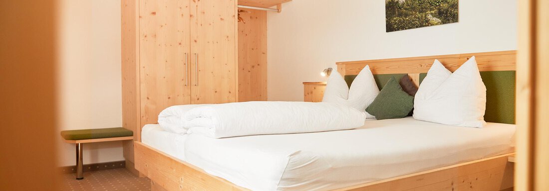 Ein gemütliches Schlafzimmer mit einem großen Bett und hellen Holzmöbeln. An der Wand hängt ein Bild von Bergen. - Gasthof Walderhof - Ochsengarten