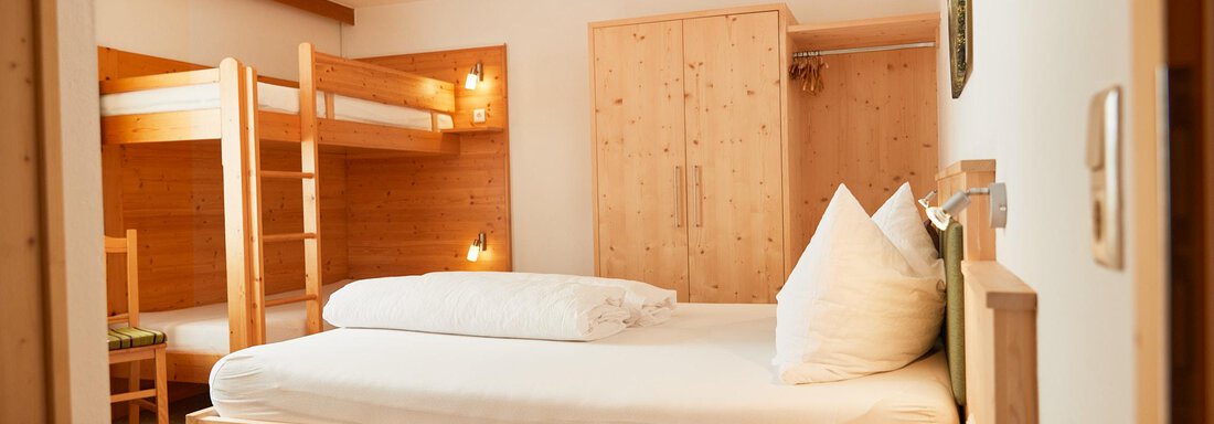 Ein modernes Zimmer mit einem Doppelbett und einem Etagenbett. Die Wände und Möbel sind aus Holz, was eine gemütliche Atmosphäre schafft. - Gasthof Walderhof - Ochsengarten