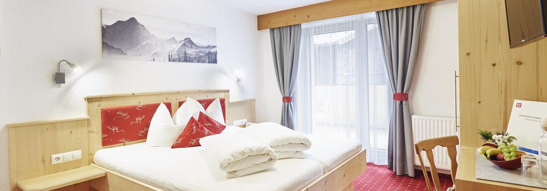 Ein gemütliches Schlafzimmer mit einem großen Bett und Holzinterieur. Der Raum hat einen Balkon mit Vorhängen und eine dekorative Wandgestaltung. - Gasthof Walderhof - Ochsengarten