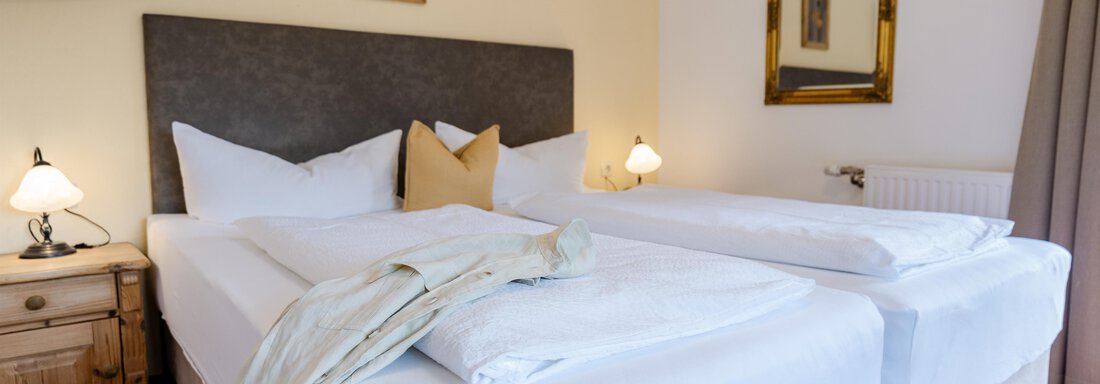 Ein gemütliches Schlafzimmer mit zwei Einzelbetten und einem warmen Ambiente. Die Wände sind in sanften Farben gehalten, und es gibt dekorative Elemente wie einen Spiegel und ein Bild. - Gasthof Waldesruh - Ochsengarten