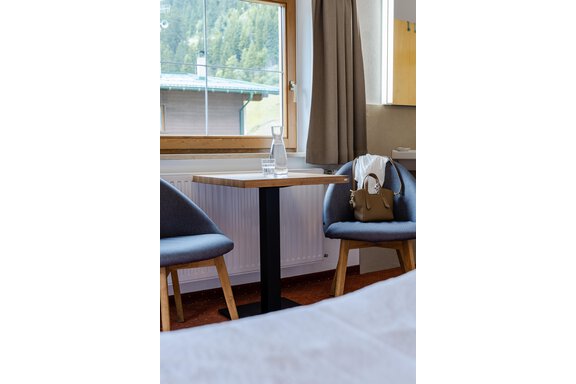 Ein gemütlicher Tisch mit zwei Stühlen neben einem Fenster. Auf dem Tisch steht eine Glas Karaffe und eine schön dekorierte Tasche liegt auf dem Stuhl. - Gasthof Waldesruh - Ochsengarten