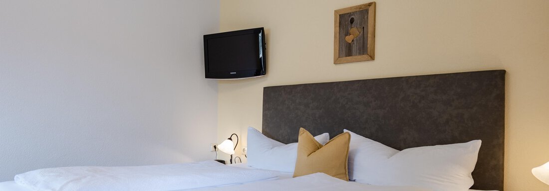 Ein helles Schlafzimmer mit zwei Einzelbetten und modernem Dekor. An der Wand ist ein Fernseher und eine kleine Kunstgalerie zu sehen. - Gasthof Waldesruh - Ochsengarten