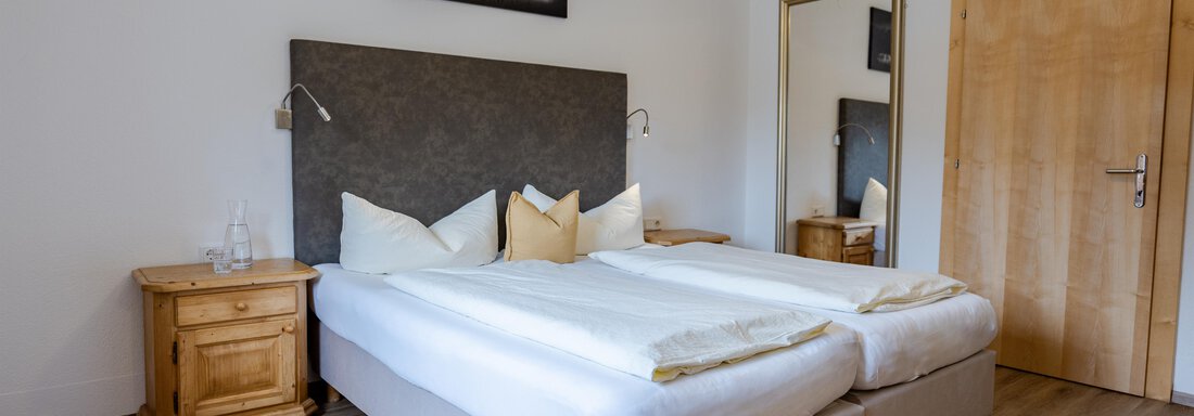 Ein modernes Schlafzimmer mit zwei Einzelbetten und einem Holzmöbel. An der Wand hängt ein Bild, und ein großer Spiegel ist sichtbar. - Gasthof Waldesruh - Ochsengarten