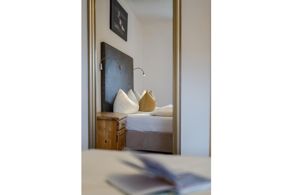 Ein gemütliches Schlafzimmer mit einem großen Bett und dekorativen Kissen. Im Hintergrund befindet sich ein Holzschrank und ein modernes Wandbild. - Gasthof Waldesruh - Ochsengarten