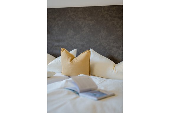 Ein bequemes Bett mit weißen und gelben Kissen. Auf der Bettdecke liegt ein geöffnetes Buch. - Gasthof Waldesruh - Ochsengarten