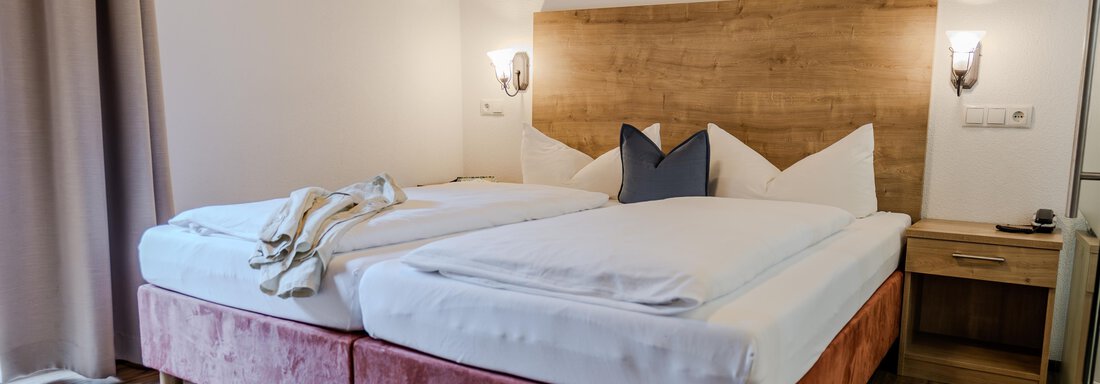 Ein gemütliches Schlafzimmer mit zwei Betten und einem Holzpaneelkopfteil. Die Einrichtung ist modern und schlicht, ideal für einen entspannten Aufenthalt. - Gasthof Waldesruh - Ochsengarten