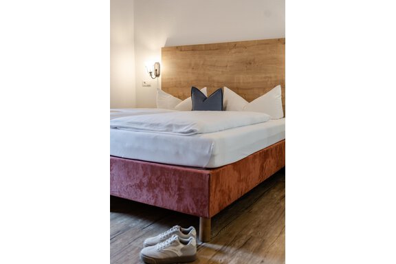 Ein gemütliches Schlafzimmer mit einem modernen Bett und Kissen. Am Fußende liegt ein Paar Sneaker auf dem Holzfußboden. - Gasthof Waldesruh - Ochsengarten