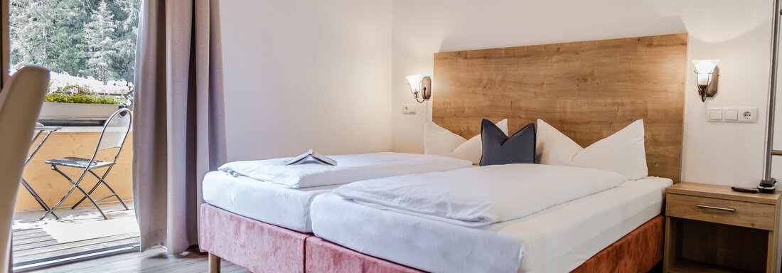 Ein gemütliches Schlafzimmer mit zwei Betten und Holzelementen. Ein Balkon mit Blick auf die Natur ist sichtbar. - Gasthof Waldesruh - Ochsengarten