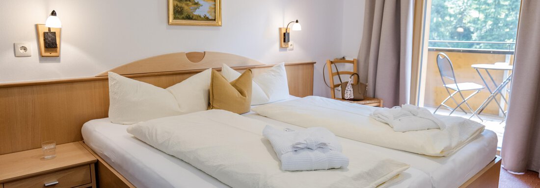 Ein gemütliches Schlafzimmer mit zwei Betten und modernen Möbeln. Neben dem Fenster befindet sich ein kleiner Balkon mit einem Tisch und Stühlen. - Gasthof Waldesruh - Ochsengarten