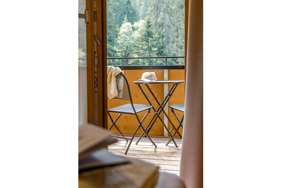 Ein gemütlicher Balkon mit zwei Stühlen und einem kleinen Tisch. Im Hintergrund sind grüne Bäume zu sehen. - Gasthof Waldesruh - Ochsengarten