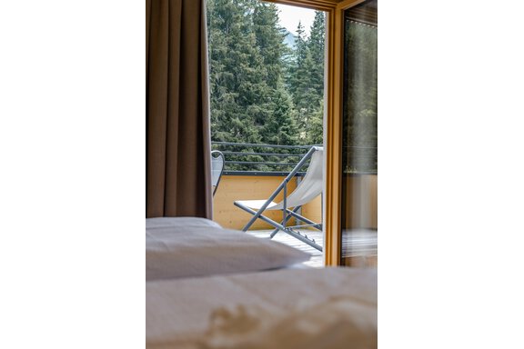 Eine gemütliche Aussicht von einem Schlafzimmer mit einem Balkon. Der Balkon ist mit einem Liegestuhl ausgestattet und umgeben von hohen Bäumen. - Gasthof Waldesruh - Ochsengarten