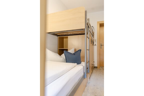 Ein helles Schlafzimmer mit einem Etagenbett und modernen Holzregalen. Auf dem Bett liegt ein blaues Kissen und die Bettwäsche ist sauber und ordentlich. - Gasthof Waldesruh - Ochsengarten