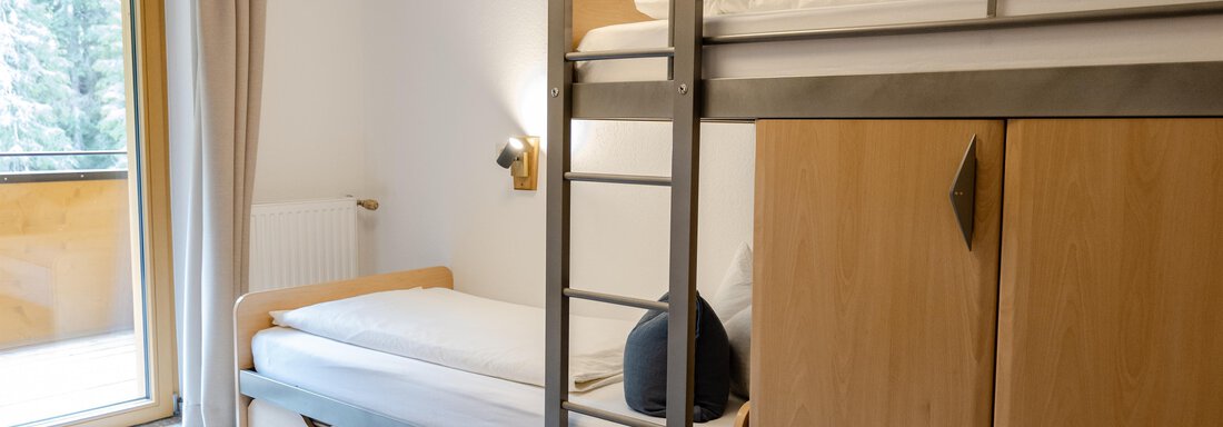 Ein gemütliches Zimmer mit einem Etagenbett und viel natürlichem Licht. Neben dem Bett befindet sich ein Holzschrank und ein Fenster mit Blick nach draußen. - Gasthof Waldesruh - Ochsengarten