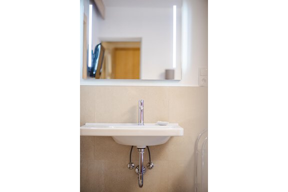 Ein modernes Waschbecken mit einem klaren Wasserhahn und Spiegel. Der Raum ist schlicht und hell gestaltet. - Gasthof Waldesruh - Ochsengarten