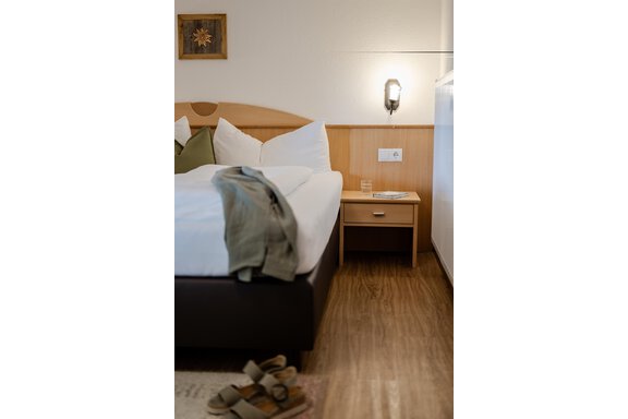 Ein gemütliches Schlafzimmer mit einem großen Bett und Kissen. Neben dem Bett steht ein Nachttisch mit einem Glas Wasser und einem Buch. - Gasthof Waldesruh - Ochsengarten