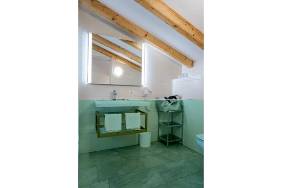 Ein modernes Badezimmer mit Holzdeckenbalken und einem beleuchteten Spiegel. Der Waschbereich ist ordentlich gestaltet, mit Handtüchern und einem praktischen Regal. - Gasthof Waldesruh - Ochsengarten