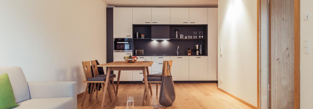 A modern kitchen-living area with a bright decor and wooden flooring. The space is cozily designed with a dining table and a seating area. - All-Suite Resort Ötztal - Oetz