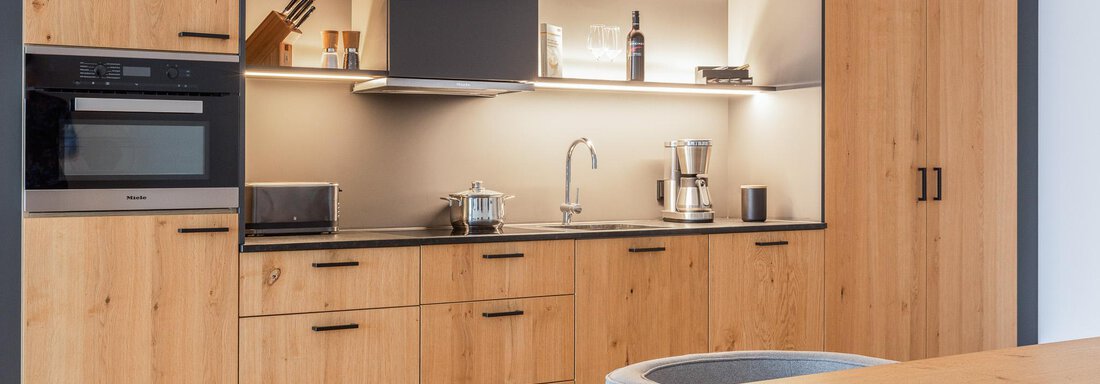 A modern kitchen with wooden cabinets and an elegant countertop. The lighting creates a pleasant atmosphere. - All-Suite Resort Ötztal - Oetz