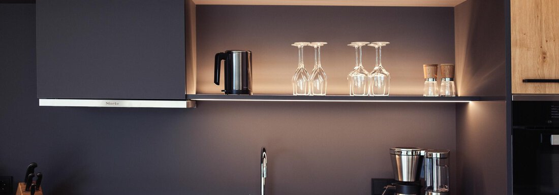 A modern kitchen with wooden cabinets and elegant appliances. On the shelf, there are glasses and a coffee machine. - All-Suite Resort Ötztal - Oetz