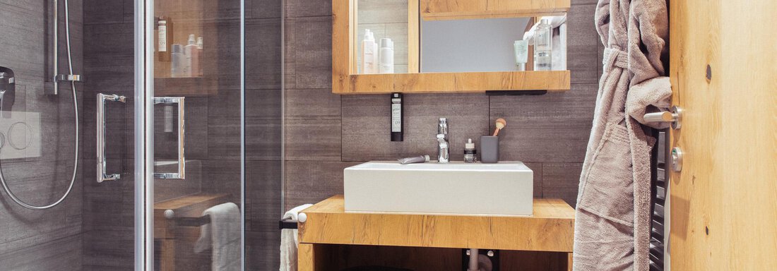 A modern bathroom with wood and glass elements. There is a shower, a sink, and a large mirror. - All-Suite Resort Ötztal - Oetz