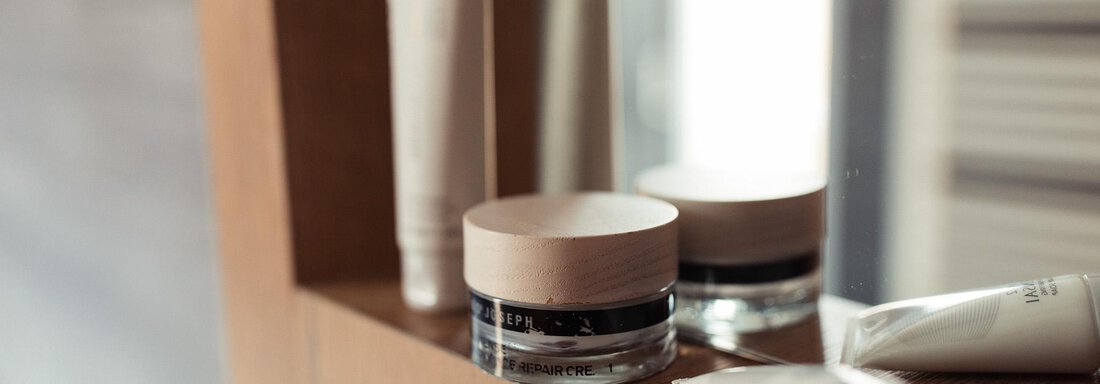 A selection of skincare products on a wooden shelf. The products consist of various tubes and a glass container with a wooden lid. - All-Suite Resort Ötztal - Oetz