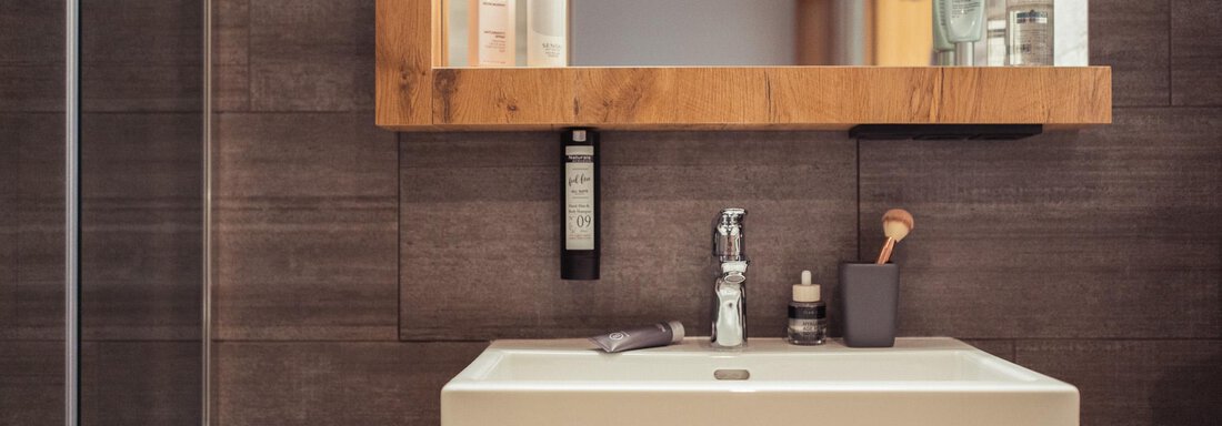 A modern bathroom with a stylish sink and a large mirror. The wooden details create a warm atmosphere. - All-Suite Resort Ötztal - Oetz