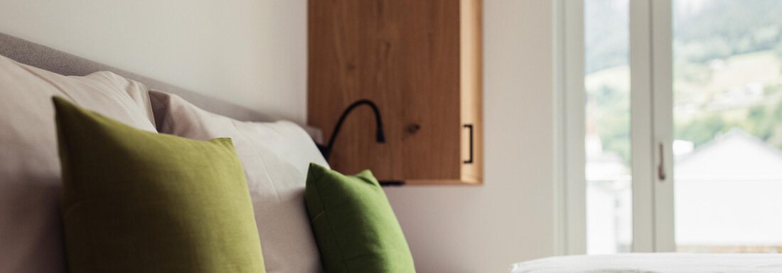 A modern bedroom with comfortable beds and green cushions. Large windows offer a view of the nature outside. - All-Suite Resort Ötztal - Oetz