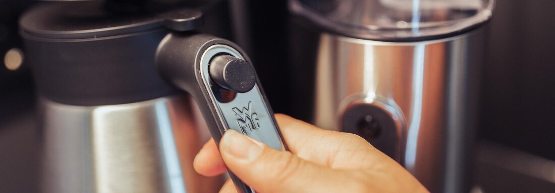 A hand operates the lever of a coffee machine. The machine has a modern, silver design. - All-Suite Resort Ötztal - Oetz