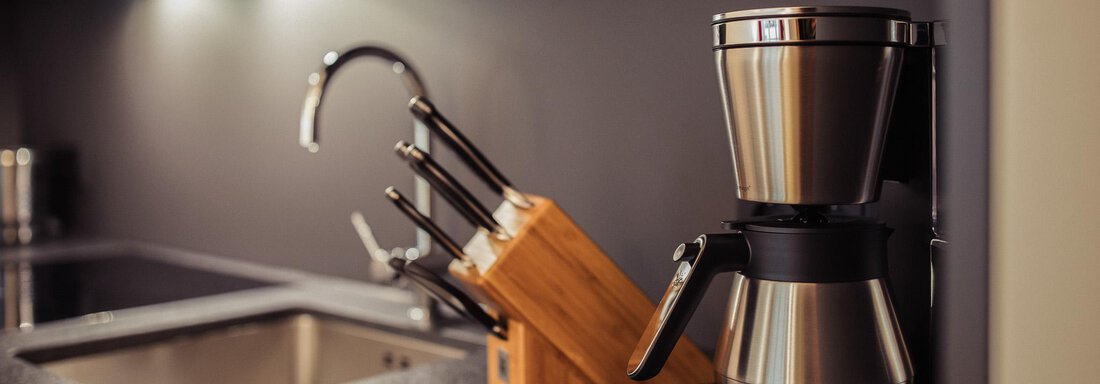 A modern kitchen with a coffee machine and a wooden block for knives. The room has an elegant, dark color scheme. - All-Suite Resort Ötztal - Oetz