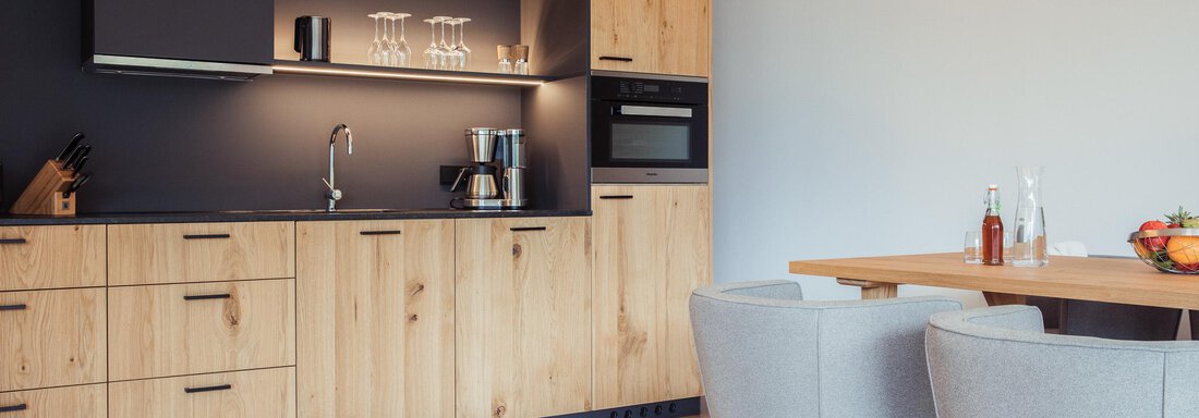 A modern kitchen with wooden furniture and elegant appliances. There are two chairs at the table and fresh fruit. - All-Suite Resort Ötztal - Oetz